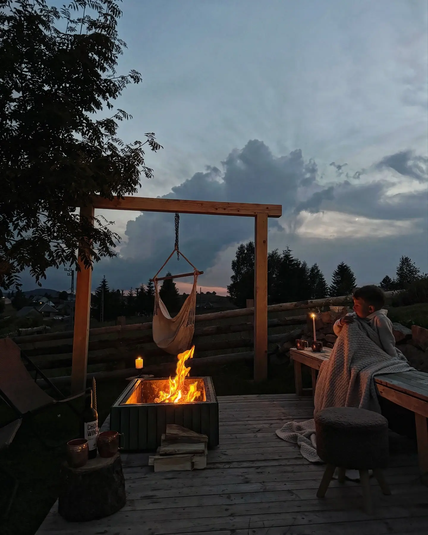Terasă cu foc de tabără, hamac și lumânări la apus